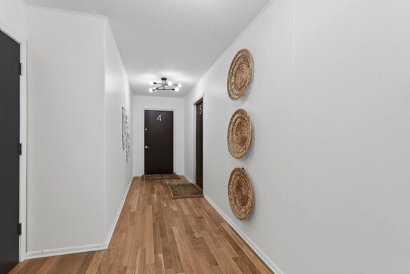 Passadís amb terra de fusta, una porta negra amb la inscripció '4' i tres penjolls murals de fibra.