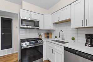 A modern kitchen with white cabinetry, a stainless steel stove, a microwave, a sink, and a dishwasher. - Designer Mid-Term Living Near Omaha Hospitals (Omaha)