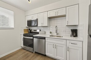 Une cuisine moderne avec des meubles blancs, des appareils en acier inoxydable et un four à micro-ondes encastré.