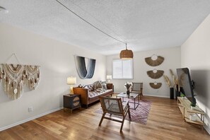 A living room with a sofa, coffee table, and chairs, a television, and decorative wall art. - Designer Mid-Term Living Near Omaha Hospitals (Omaha)