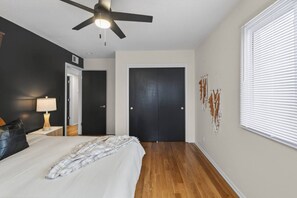 A bedroom with a bed, a nightstand, a lamp, a ceiling fan, and a door. - Designer Mid-Term Living Near Omaha Hospitals (Omaha)
