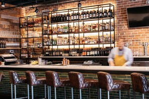 A bar with leather bar stools, a brick wall, and shelves of bottles. - Prime Location Midtown Omaha (Omaha)