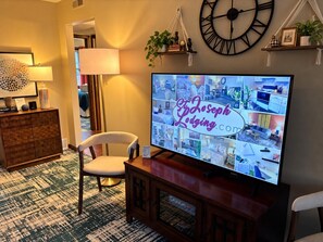 Una televisione che mostra un sito web, una sveglia, una sedia, una lampada e un tappeto decorato.