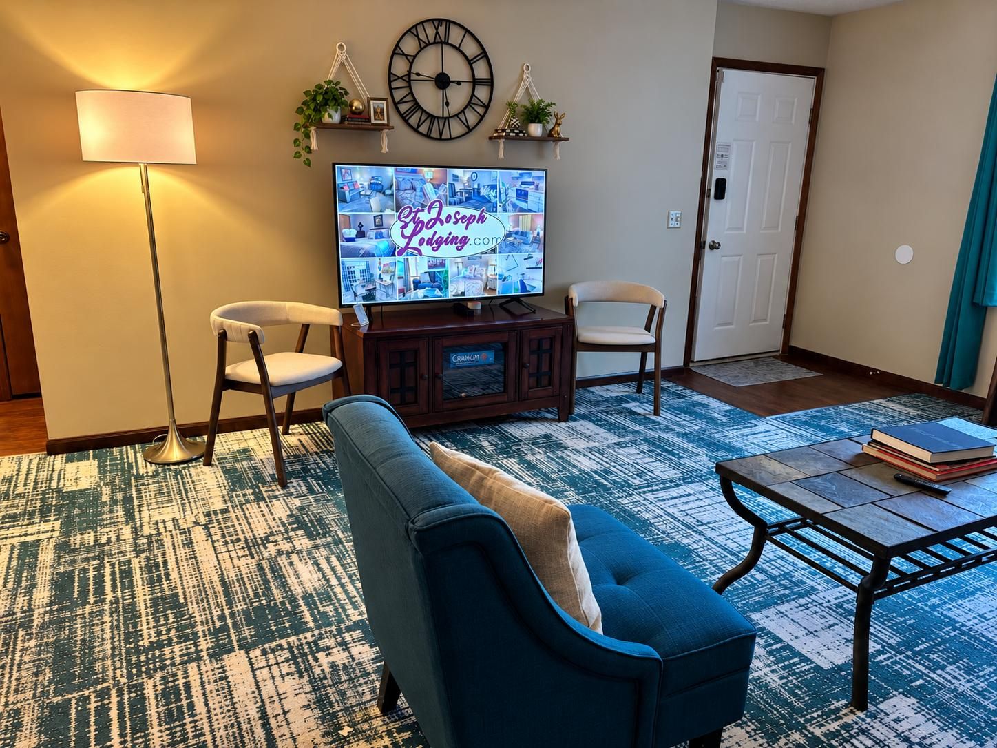 Ein Wohnzimmer mit Fernseher, zwei Sessel, einem Sofa, einem Couchtisch und einem gemusterten Teppich.