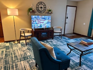 Ein Wohnzimmer mit Fernseher, zwei Sessel, einem Sofa, einem Couchtisch und einem gemusterten Teppich.