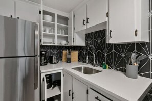 Una cocina moderna con armarios blancos, un refrigerador de acero inoxidable, un salpicadero blanco y negro y un lavabo con grifo.