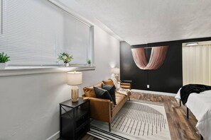 A modern bedroom with a bed, a sofa, a lamp, and a wall-mounted hanging. - Prime Location Midtown Omaha (Omaha)
