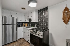 A modern kitchen with white cabinets, a stainless steel refrigerator, a gas stove, and a black and white backsplash. - Prime Location Midtown Omaha (Omaha)