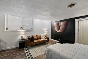 Quarto moderno com cama, sofá, janela com persianas, cadeira suspensa e porta.