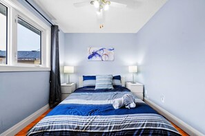 A bedroom with a bed, two bedside tables, a ceiling fan, a window with curtains, and a painting on the wall. - Comfy Getaway - Walk to West Ed Mall (Edmonton)