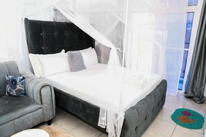 A bedroom with a bed under a canopy, a grey sofa, and a pet bed on the floor. - Modern Studio In Mtwapa, Kenya (Mtwapa)