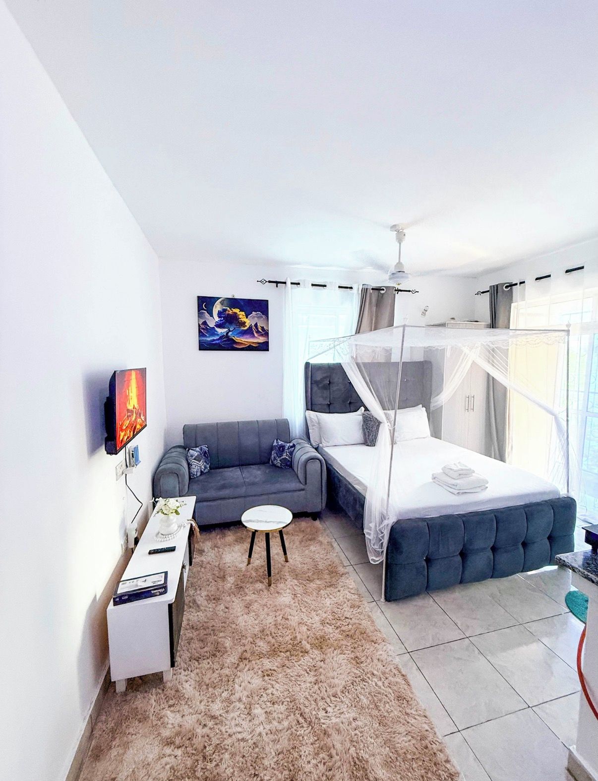 Une chambre à coucher moderne avec un lit, un canapé, un téléviseur et un tableau accroché au mur.