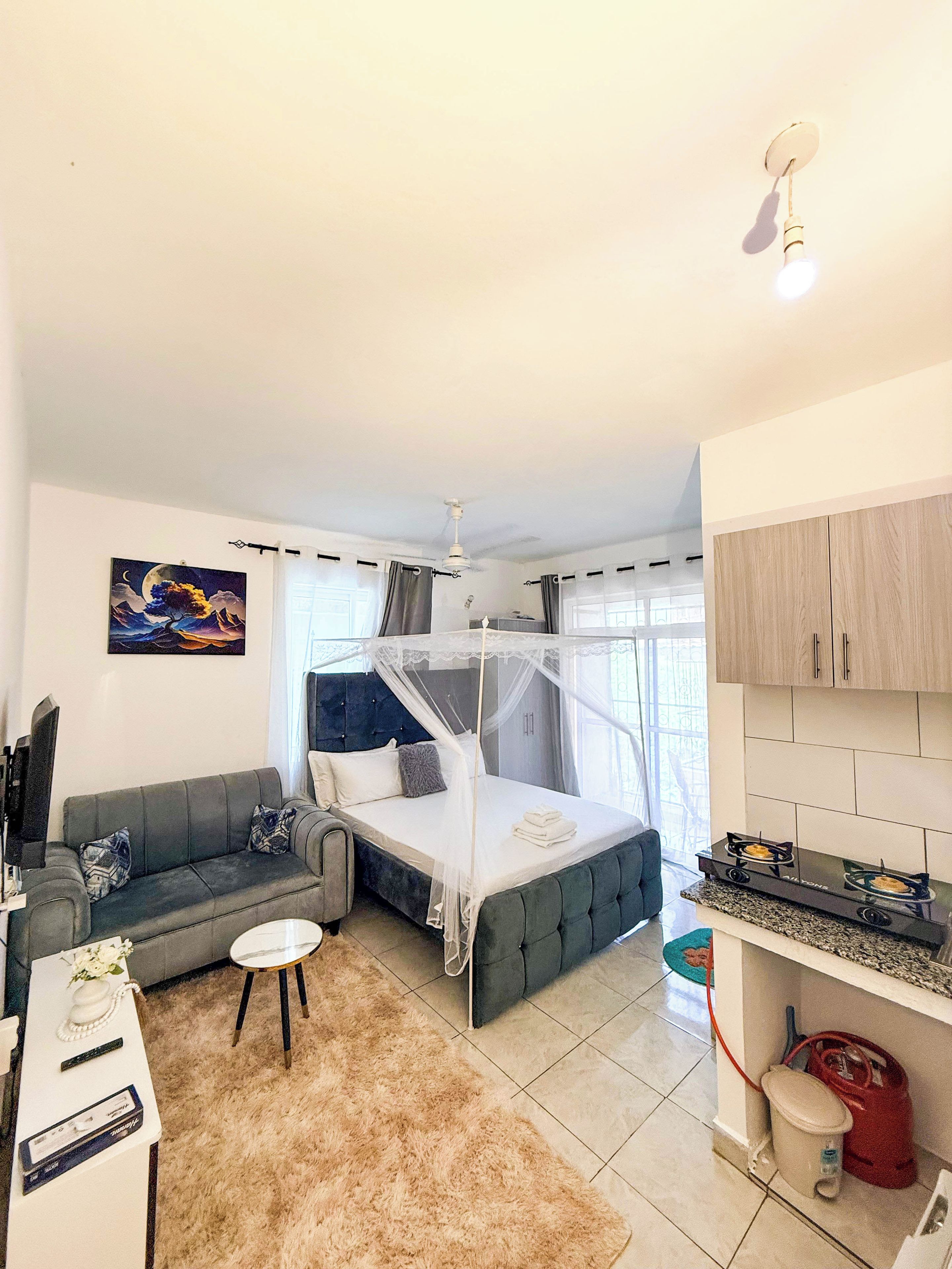 Habitación de hotel compacta con cama, sofá, mesita, televisor y kitchenette.