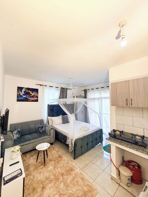 A compact hotel room with a bed, a sofa, a small table, a TV, and a kitchenette. - Modern Studio In Mtwapa, Kenya (Mtwapa)