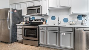Una cocina con electrodomésticos de acero inoxidable, armarios blancos, microondas, horno y lavavajillas.