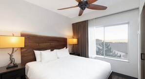 Une chambre d’hôtel avec un grand lit, deux lampes de chevet, un ventilateur de plafond et une fenêtre donnant sur un beau paysage.