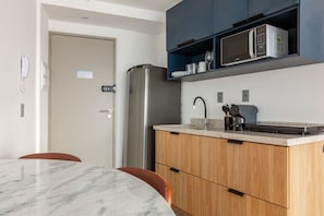 A modern kitchen with a refrigerator, microwave, and a built-in oven. There is a wooden cabinet with a countertop, and a marble table with chairs. - Niemeyer 360 (Rio de Janeiro)