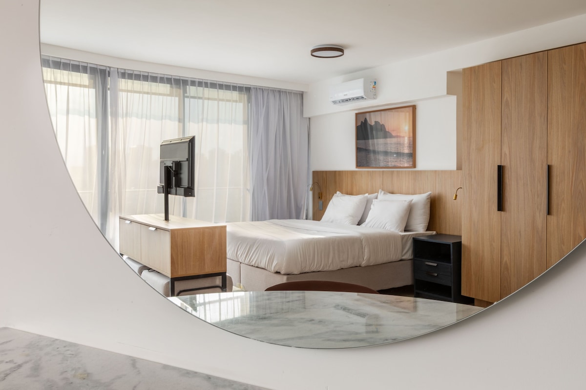A modern hotel room with a bed, a desk, a TV, and a wardrobe.
