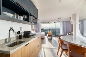 A modern kitchen with a built-in microwave, a coffee maker, and a sink. There is a dining area with a table and chairs, and a large window offering a city view. - Niemeyer 360 (Rio de Janeiro)