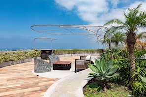 An outdoor seating area with a view of the ocean, featuring a metal pergola, wicker chairs, and a wooden table. - Niemeyer 360 (Rio de Janeiro)