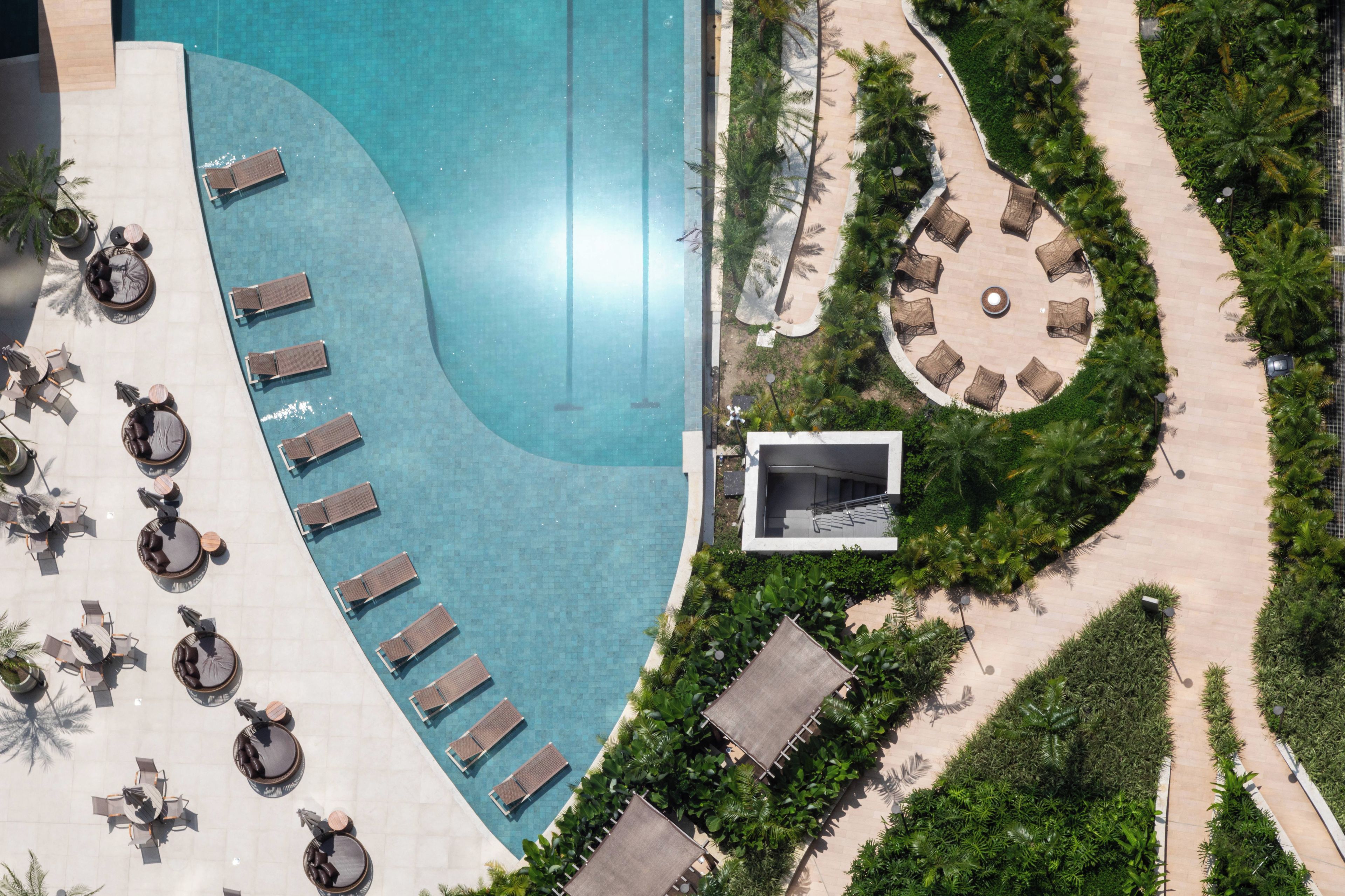 An aerial view of a resort with a swimming pool, sun loungers, and a circular seating area surrounded by greenery.