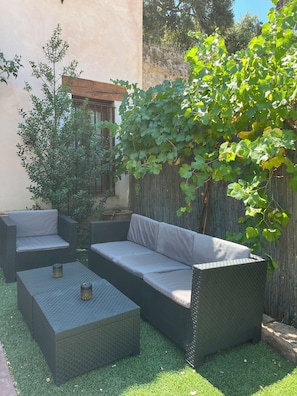 A patio area with a wicker sofa, two square tables, and a small tree.