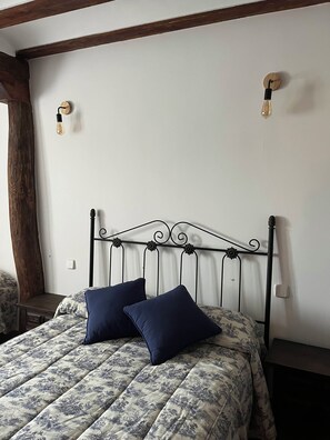 A bed with a floral-patterned duvet and two pillows, a wooden headboard, and two wall-mounted light fixtures.