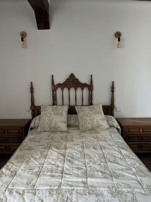 A bed with a floral patterned bedspread, wooden headboard, and two bedside tables with lamps.