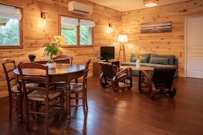 A cozy wooden interior with a dining table, chairs, a sofa, and a television. - Chalet du Courlis - VENDAYS MONTALIVET (VENDAYS MONTALIVET)