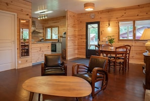 A wooden interior with a dining area, chairs, a table, a kitchen with an oven, and a door leading outside. - Chalet du Courlis - VENDAYS MONTALIVET (VENDAYS MONTALIVET)
