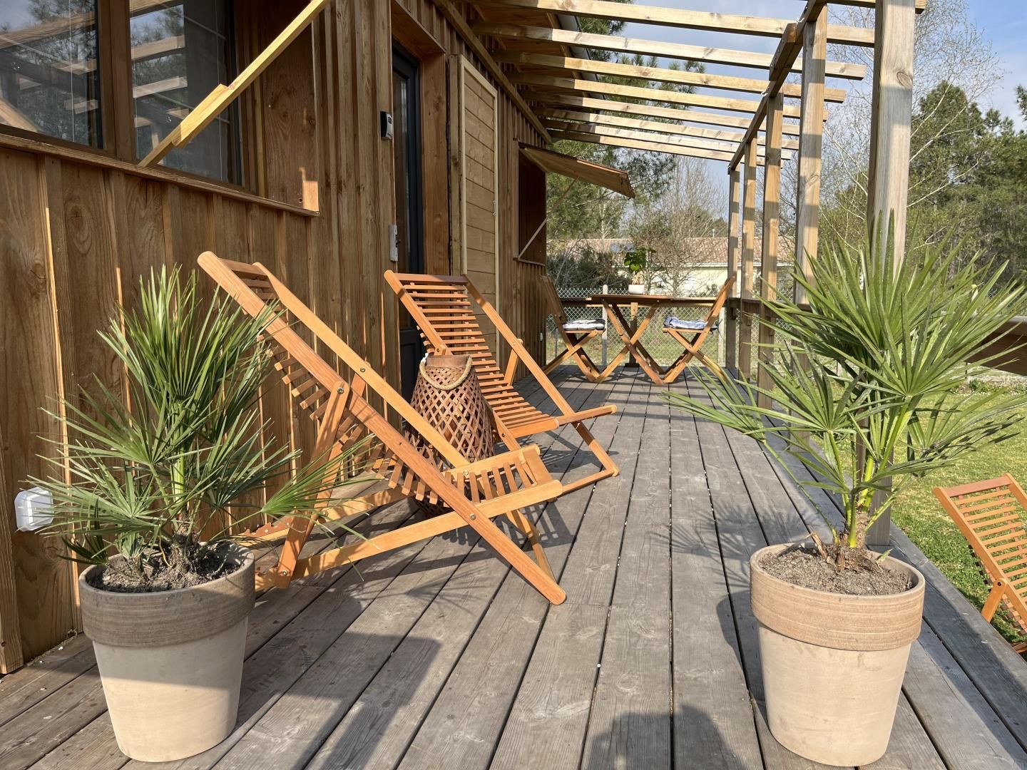 Une terrasse en bois avec deux chaises longues et des plantes en pot.