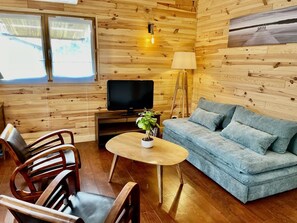 A cozy room with a wooden interior, a sofa, a television, a lamp, and a table with a plant. - Chalet du Courlis - VENDAYS MONTALIVET (VENDAYS MONTALIVET)