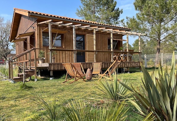 A wooden cabin with a balcony, outdoor seating, and a garden. - Chalet du Courlis - VENDAYS MONTALIVET (VENDAYS MONTALIVET)