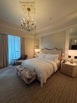 A hotel room with a large bed, a sitting area with a chair, a small table, and a nightstand with a lamp. - Timeless 1 Bedroom Suite Luxury at The Iconic St. Regis New York (New York)