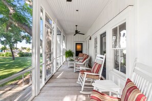 Eine überdachte Veranda mit weißen Geländern, Korbmöbeln und einem Deckenventilator.