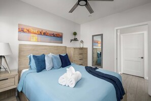 Een hotelkamer met een bed, nachtkastje, lamp, schilderij, spiegel en een deur.
