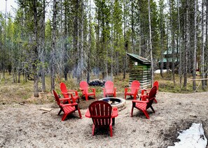 Ein Wald mit einer rustikalen Holzhütte und roten Adirondack-Stühlen, die um eine Feuerstelle angeordnet sind.