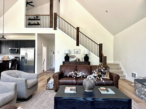 Ein geräumiges Wohnzimmer mit hoher Decke, einer Treppe und einer Küche im Hintergrund.