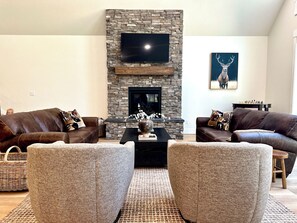 Una sala de estar con chimenea de piedra, sofás de cuero y un televisor de pantalla plana.