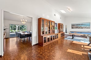 A spacious room with a wooden floor, a dining area with chairs, a pool table, and a large window with a view. - Renovated La Jolla Villa: Ocean Views & Pool (San Diego)