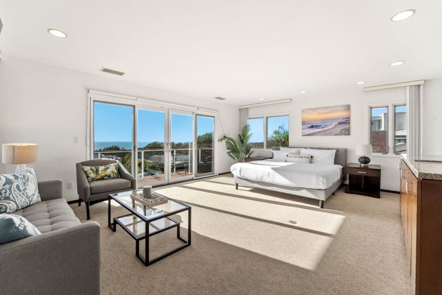 Une chambre moderne avec un grand lit, un canapé, une table basse et une vue sur l’océan par les grandes portes coulissantes.