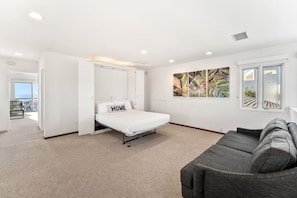 A bedroom with a bed, a gray sofa, a window, and a view of the outdoors. - Renovated La Jolla Villa: Ocean Views & Pool (San Diego)