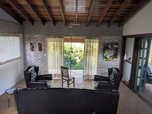 A room with a brick wall, a wooden ceiling, a large window with curtains, a wooden chair, and a sofa. - Awesome 2-bedroom chácara in peaceful Delfim Moreira getaway (Delfim Moreira)