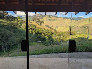 A view from a covered area with a dirt floor, overlooking a hilly landscape with trees and a small building. - Awesome 2-bedroom chácara in peaceful Delfim Moreira getaway (Delfim Moreira)