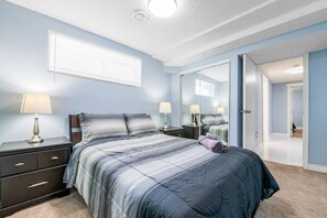 Un dormitorio con cama, mesitas de noche, un espejo y una puerta que da a otra habitación.