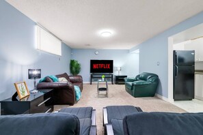 A living room with a flat-screen TV, leather sofas, a coffee table, and a refrigerator. - 2BR Suite - 4 Min Walk to WEM - Free Parking (Edmonton)
