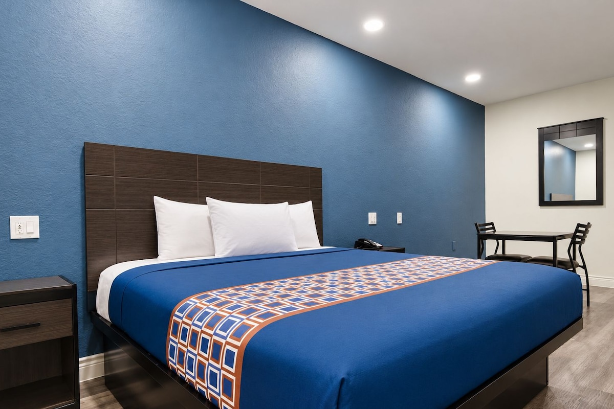A hotel room with a bed, bedside table, and a desk with chairs.