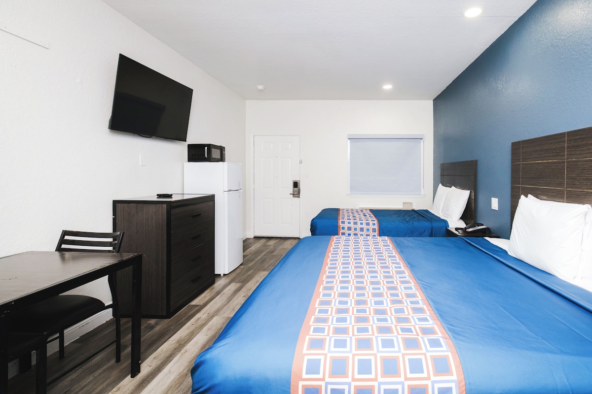 A hotel room with a bed, a desk, a chair, a television, and a window.
