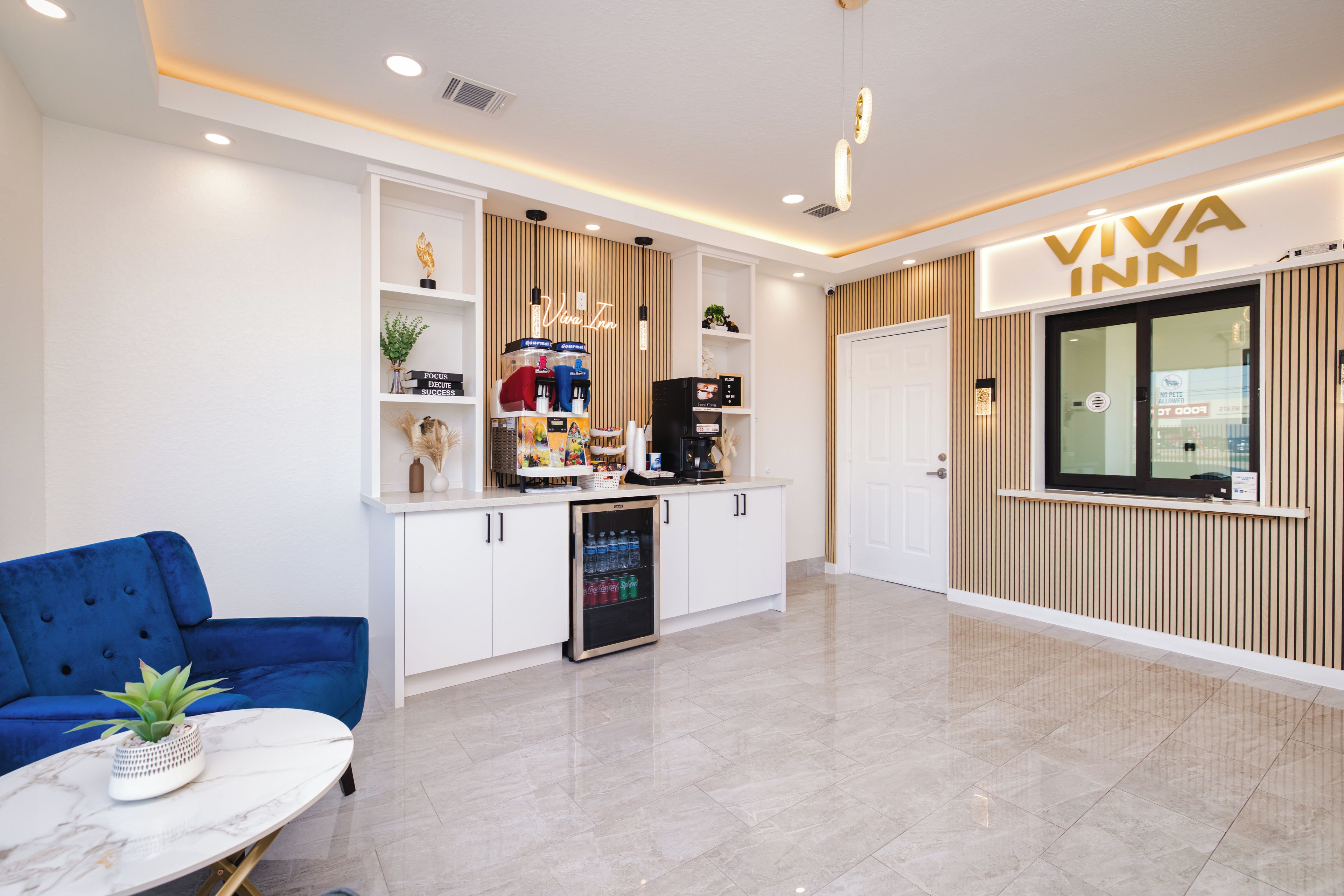 Un moderno vestíbulo de hotel con mostrador de recepción, zona de estar con un sofá azul, minibar y máquina de café.