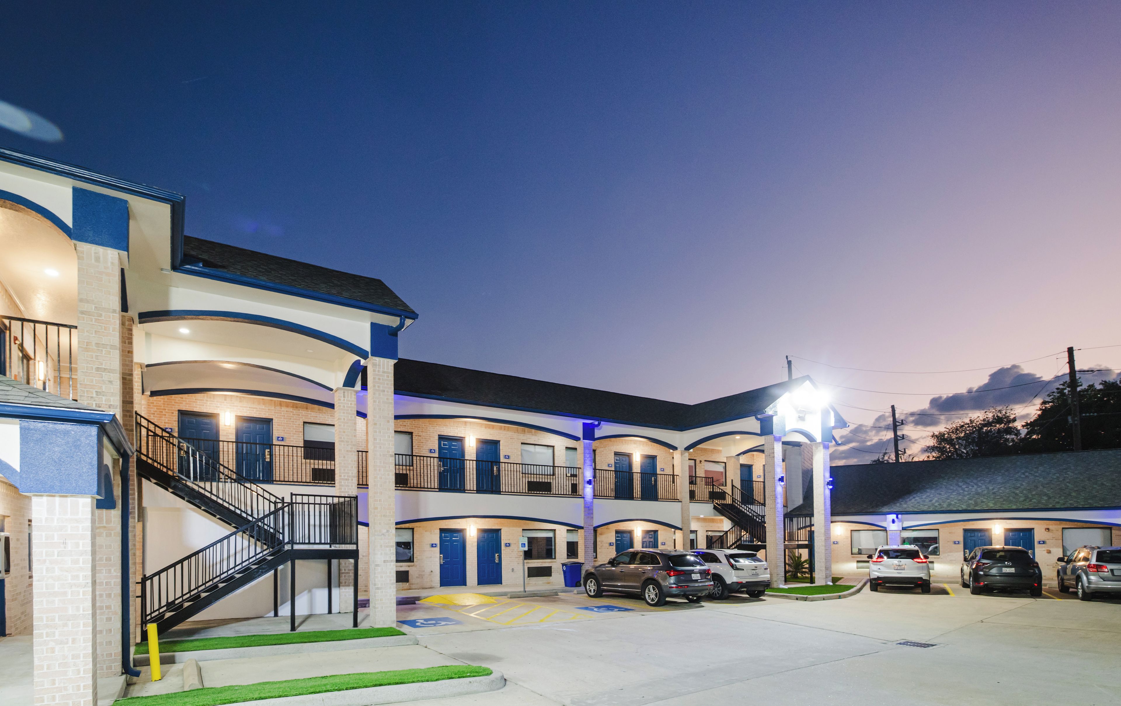 Un motel à plusieurs étages doté d’une cour intérieure, d’un parking extérieur et d’un escalier menant aux niveaux supérieurs.